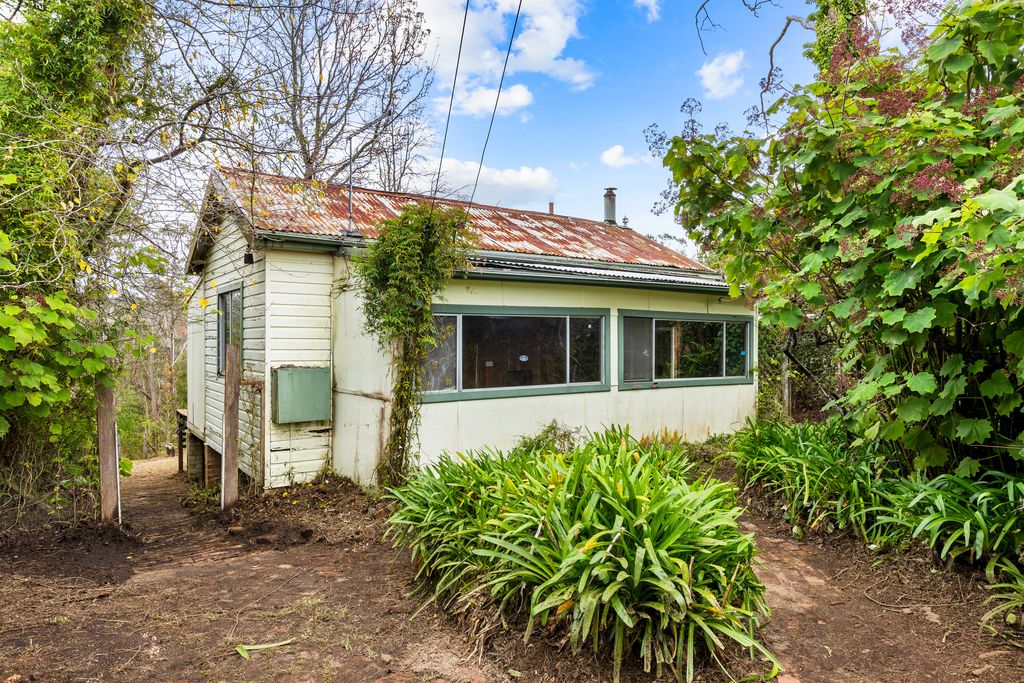 The weatherboard cottage at 23 Genevieve Road with a rusted iron roof, a row of windows and garden beds along the path